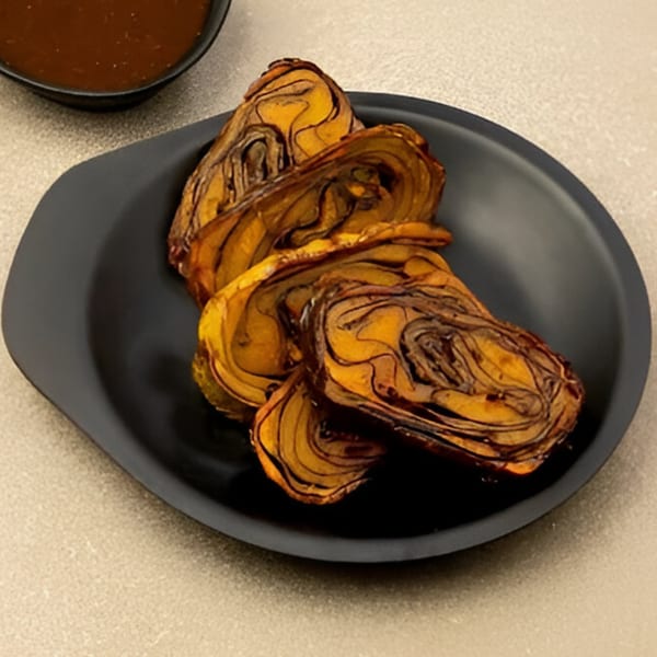 Several pieces of Turmerica's Indian snack, Patra, are arranged on a black plate with a sauce bowl.