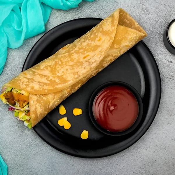 Turmerica's Indian chicken wrap with corn, lettuce, and sauce on a black plate.