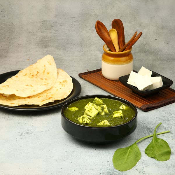 Palak Paneer with flatbreads, fresh paneer cubes, and spinach leaves on a gray surface.