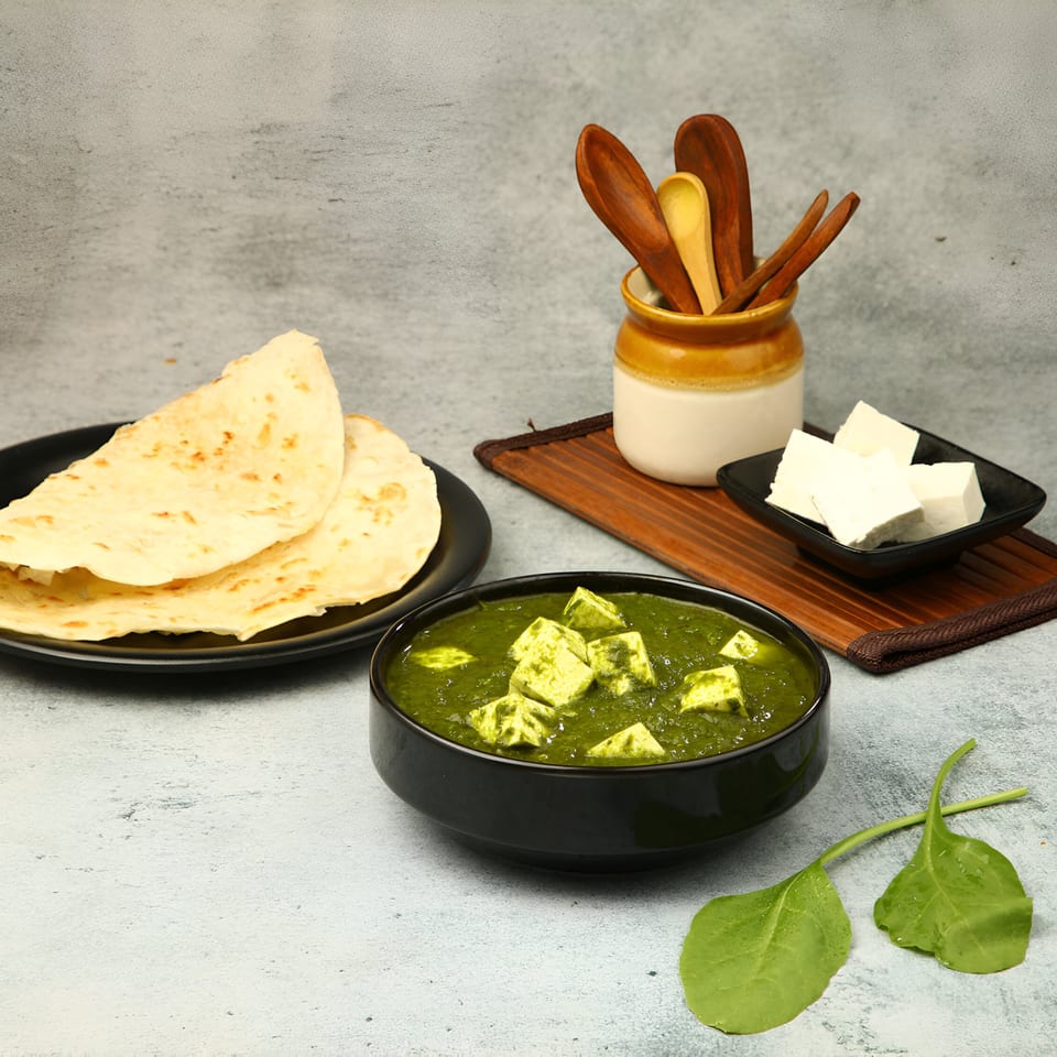 Palak Paneer with flatbreads, fresh paneer cubes, and spinach leaves on a gray surface.
