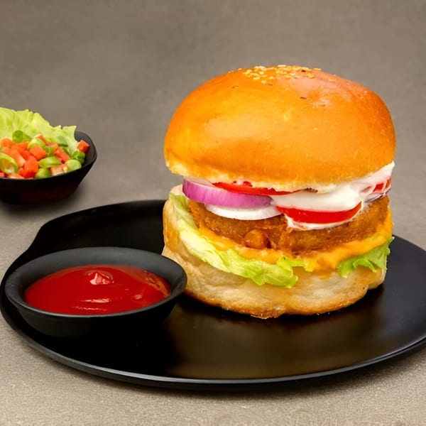 A Turmerica Indian burger with a crispy patty, lettuce, onion, tomato, and sauces, served with ketchup and salad.