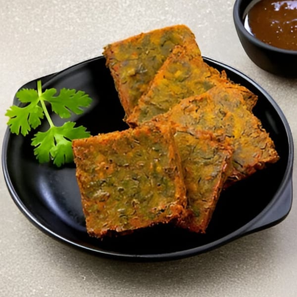 Four square pieces of green and orange Indian food, garnished with cilantro, on a black plate.
